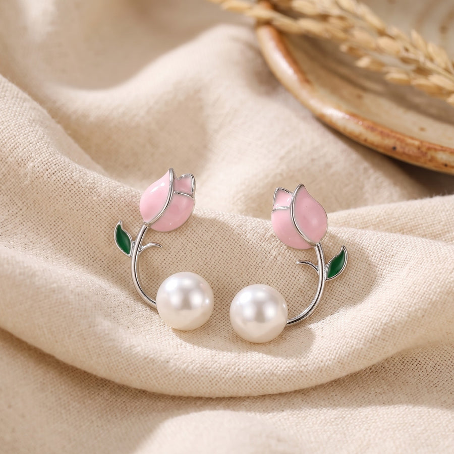 A pair of silver-tone stud earrings designed as pink tulips with green leaves and white pearl-like drops, displayed on draped beige fabric. - PALLORE Jewellery